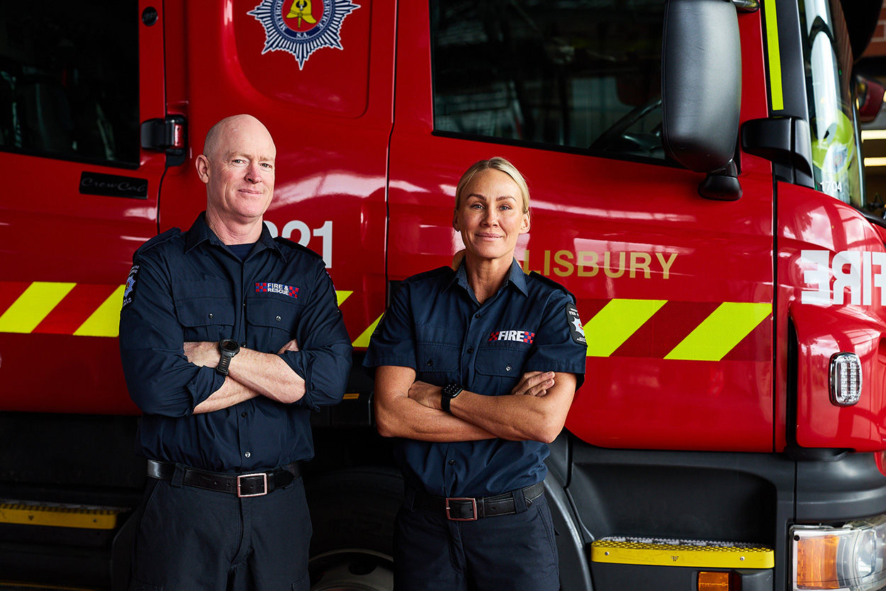 Two firefighters standing in front of a fire truck.