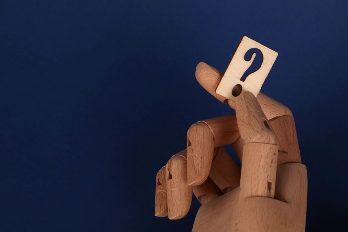 Wooden hand holding a question mark tile. 